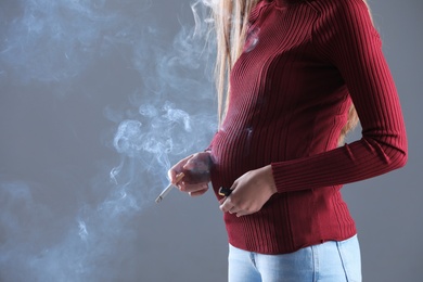 Photo of Young pregnant woman smoking cigarette on grey background, closeup. Space for text