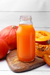 Tasty pumpkin juice in glass bottle and pumpkins on white wooden table