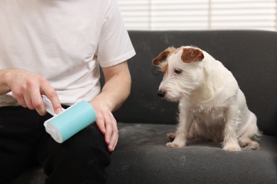 Photo of Pet shedding. Man with lint roller removing dog's hair from pants at home, closeup