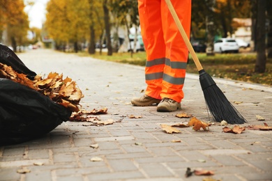 Photo of Street cleaner sweeping fallen leaves outdoors on autumn day, closeup