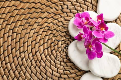 Photo of Spa stones and orchid flowers on wicker mat, top view. Space for text