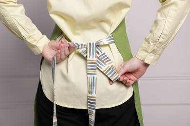 Photo of Woman putting on green apron against white wall, closeup