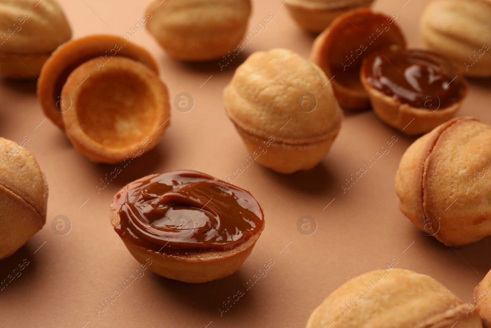 Photo of Homemade walnut shaped cookies with boiled condensed milk on pale brown background, closeup