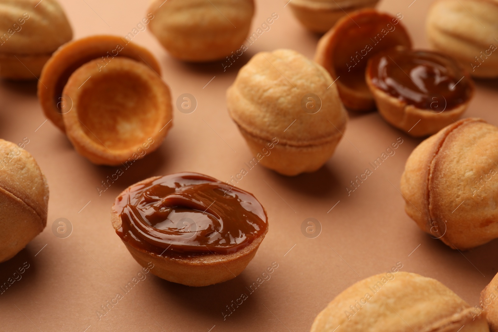 Homemade walnut shaped cookies with boiled condensed milk on pale brown background, closeup Photo of Homemade walnut shaped cookies with boiled condensed milk on pale brown background, closeup