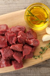 Photo of Pieces of raw beef meat, oil and garlic on wooden table, top view