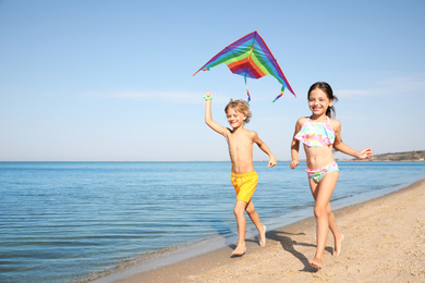 Photo of Cute little children with kite running at sandy beach on sunny day
