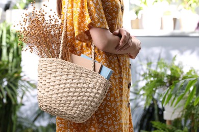 Woman holding beach bag with books and beautiful bouquet of dried flowers indoors, closeup