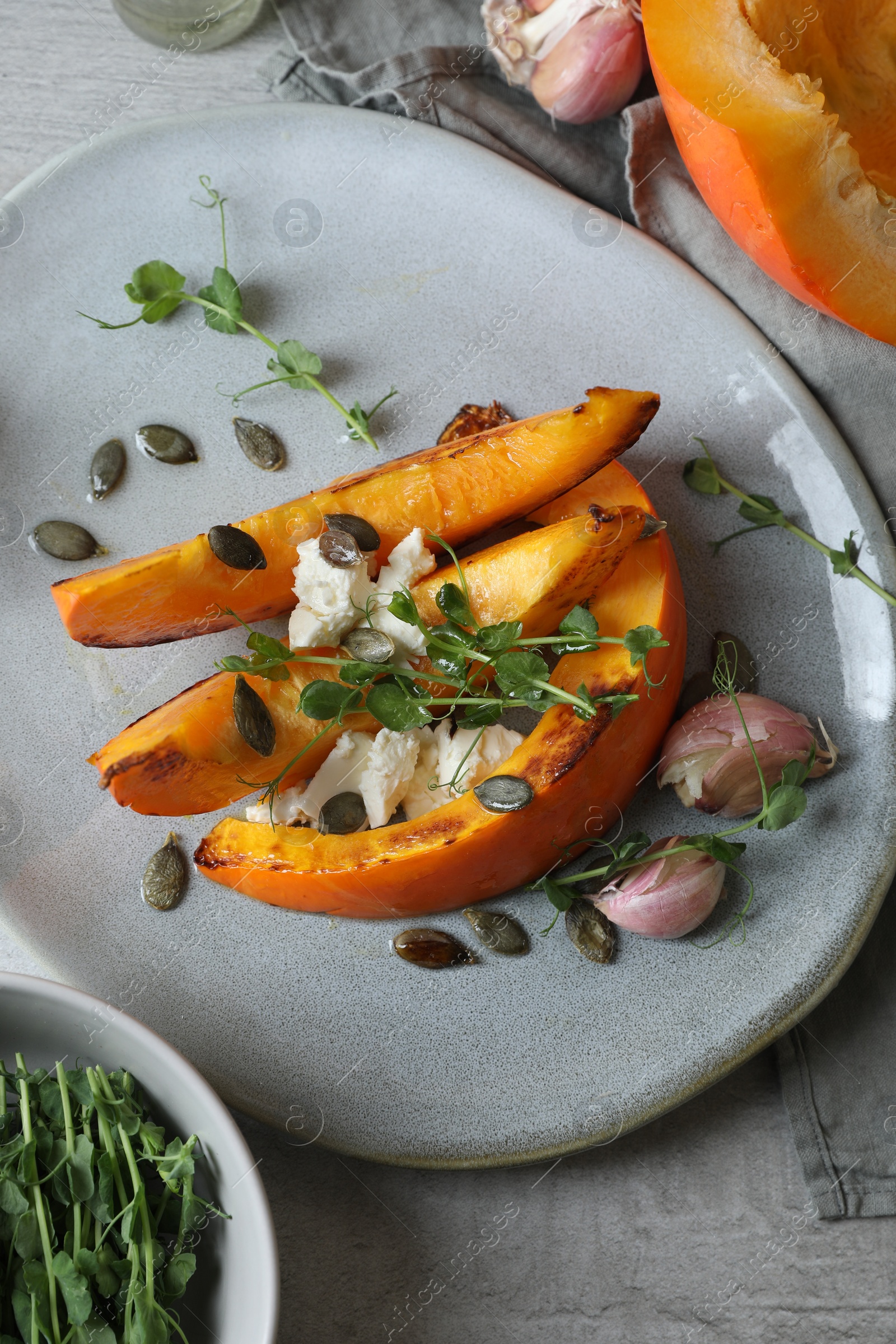 Photo of Baked pumpkin slices served with cheese, microgreens, seeds and garlic on light table, above view