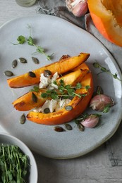 Photo of Baked pumpkin slices served with cheese, microgreens, seeds and garlic on light table, above view