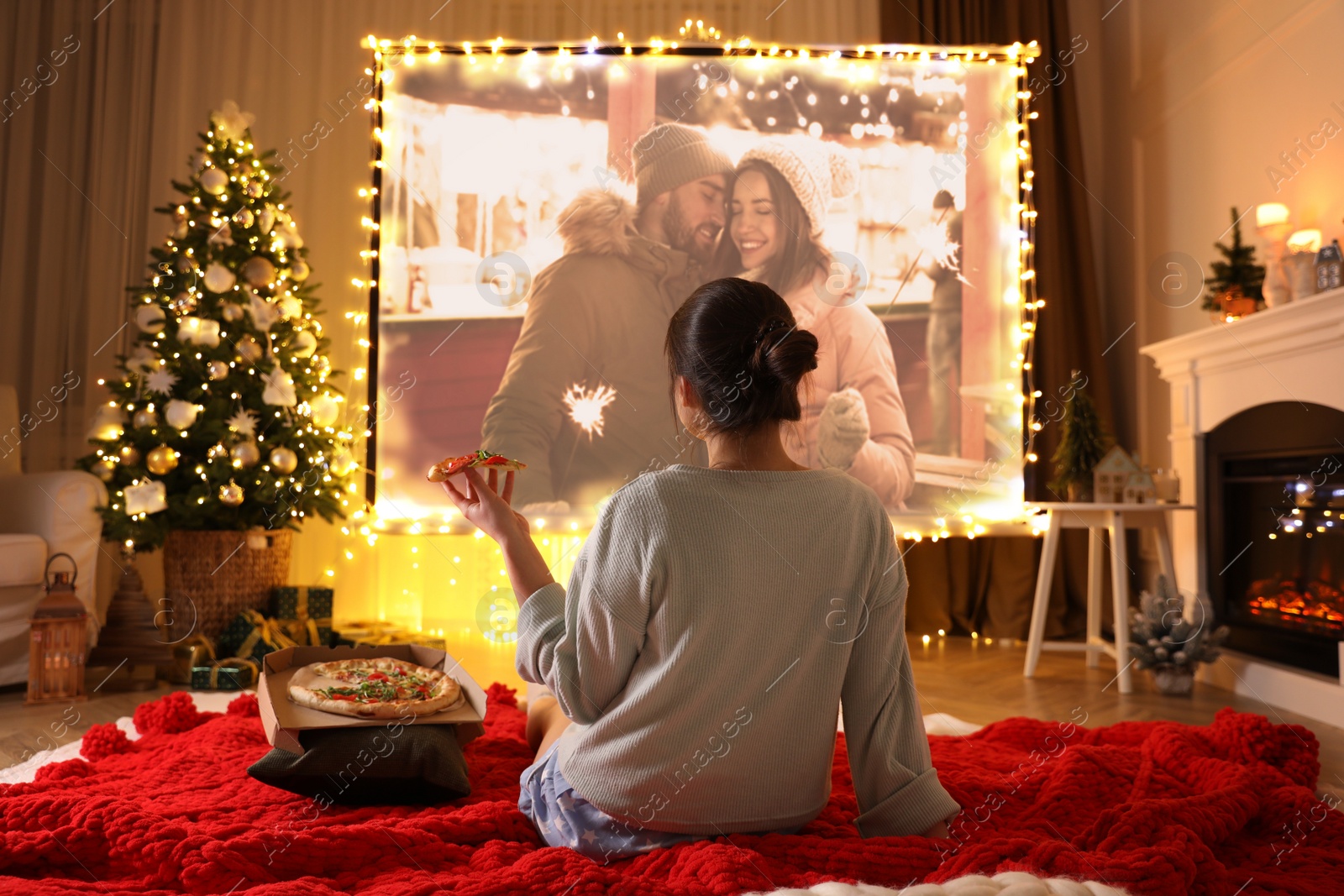 Image of Woman eating tasty and watching romantic Christmas movie via video projector in room. Cozy winter holidays atmosphere