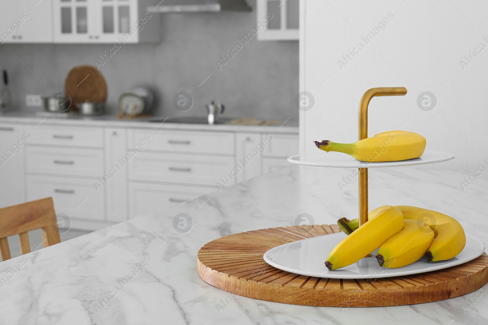 Photo of Fruit stand with bananas on white marble table in kitchen. Interior design\