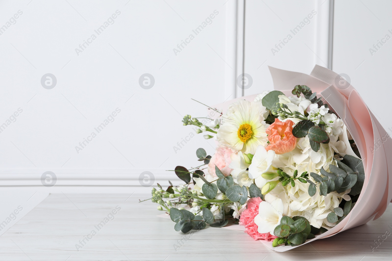 Photo of Bouquet of beautiful flowers on wooden table near white wall. Space for text