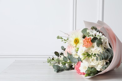 Photo of Bouquet of beautiful flowers on wooden table near white wall. Space for text