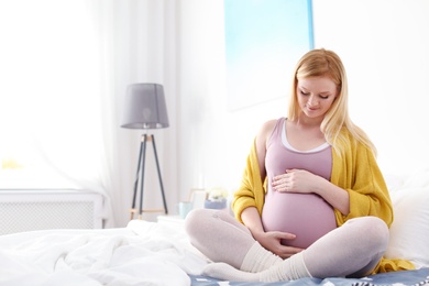 Photo of Beautiful pregnant woman sitting on bed in light room. Space for text