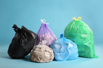 Different trash bags full of garbage on light blue background