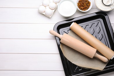 Photo of Baking pan with parchment paper, different ingredients and kitchen tools on white wooden table, flat lay. Space for text