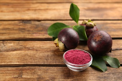 Photo of Purple mangosteen powder and fruits on wooden table. Space for text