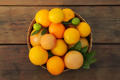 Wicker basket with different citrus fruits and leaves on wooden table, top view
