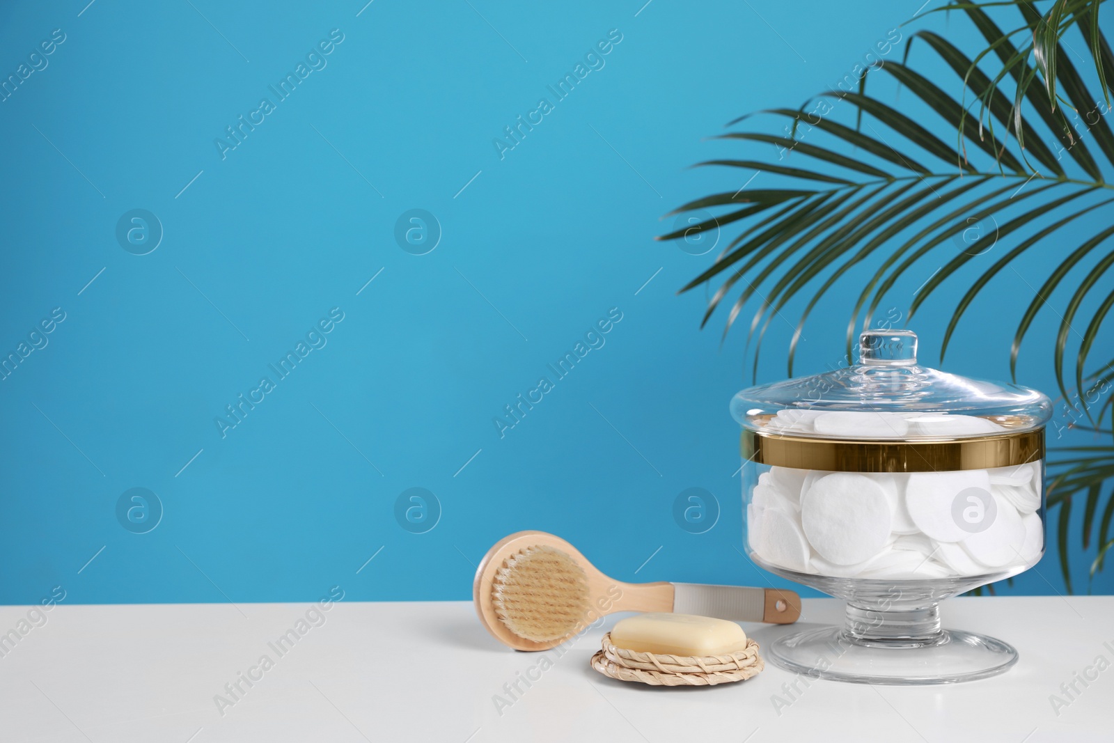 Photo of Jar with cotton pads on white table against blue background. Space for text