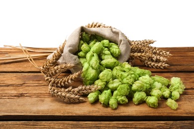 Photo of Overturned sack of hop flowers and wheat ears on wooden table against white background