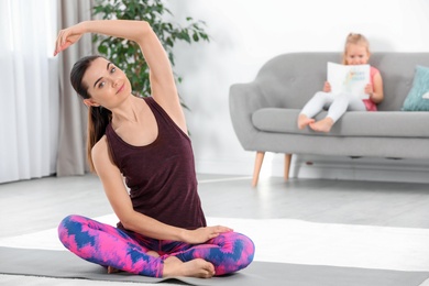 Photo of Woman doing fitness exercises while her daughter sitting on sofa at home