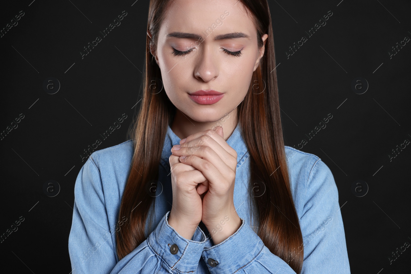 Photo of Woman with clasped hands praying on black background