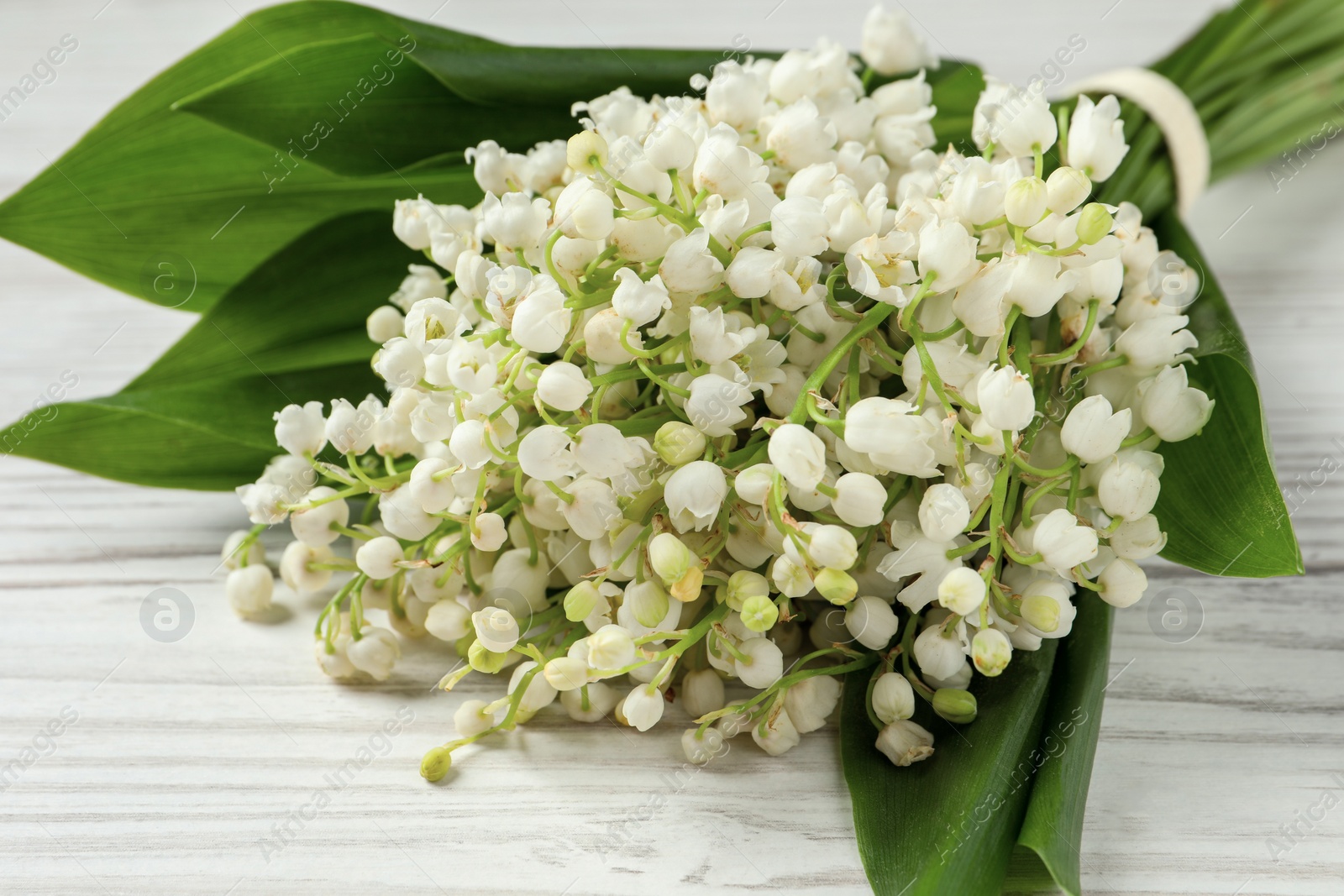 Photo of Beautiful lily of the valley bouquet on white wooden table, closeup