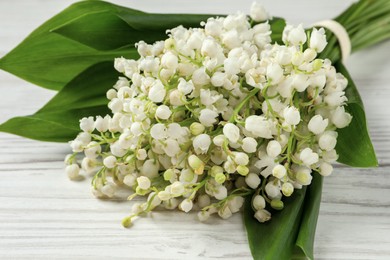 Photo of Beautiful lilythe valley bouquet on white wooden table, closeup