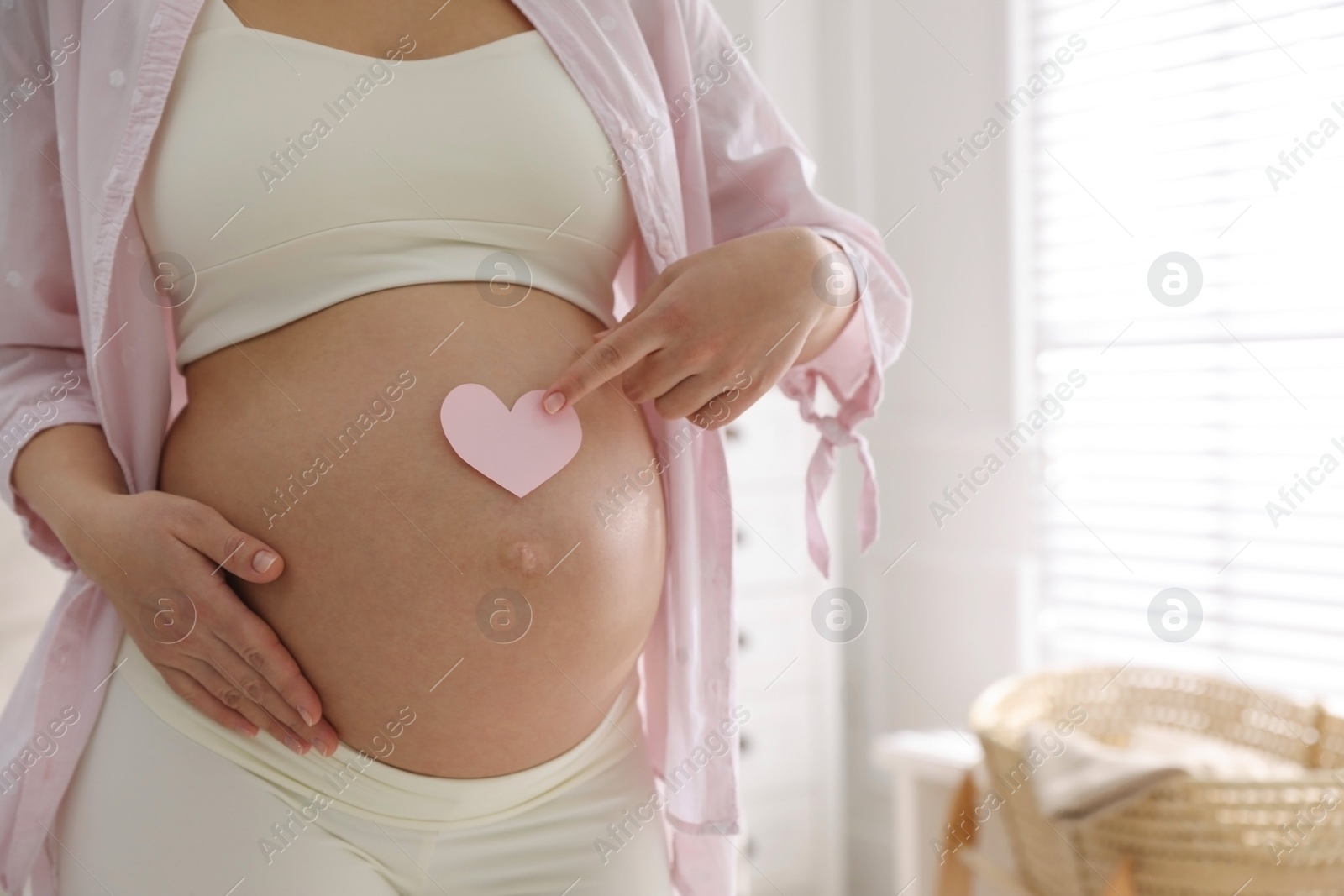 Photo of Pregnant woman with heart shaped sticky note on belly indoors, closeup. Choosing baby name