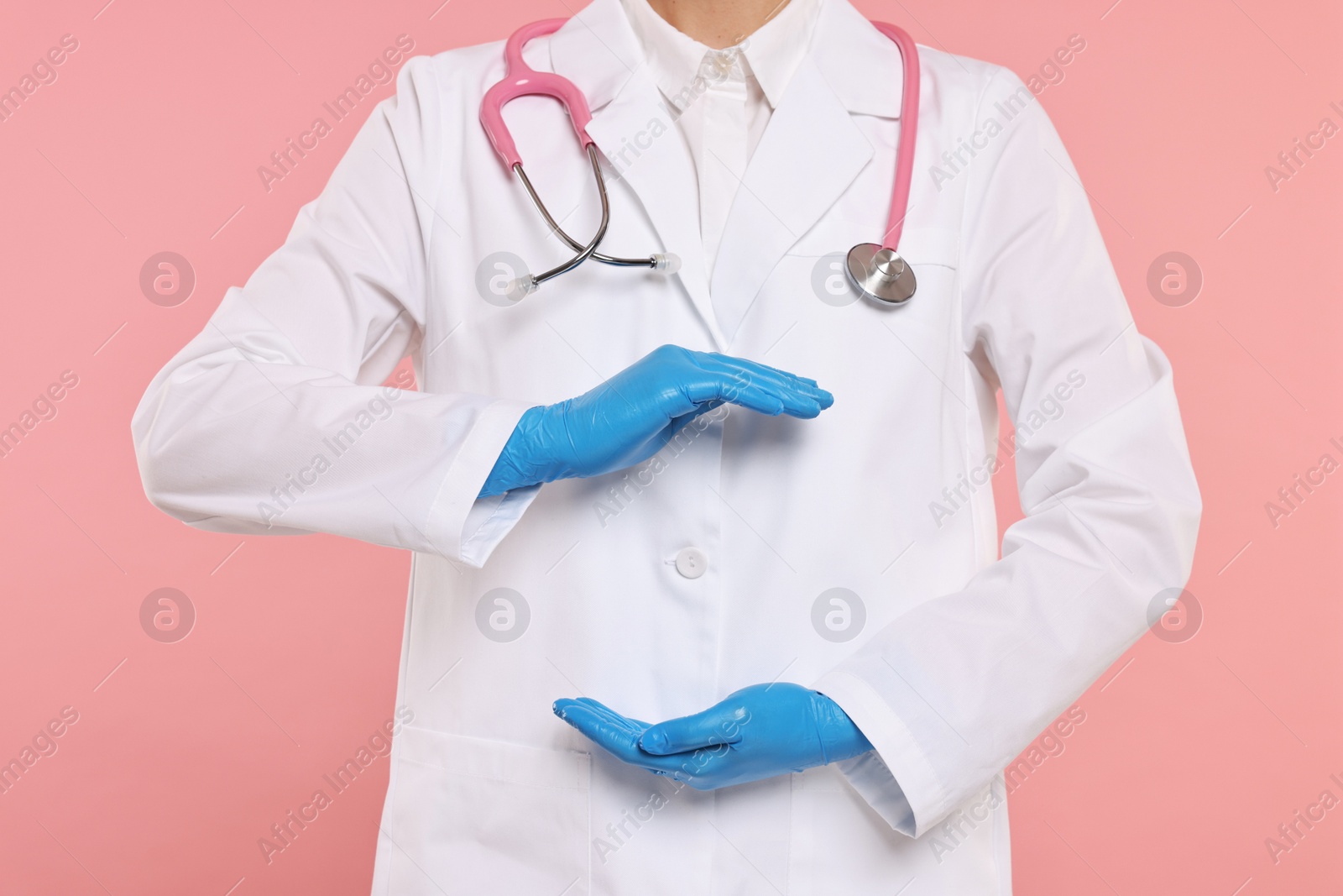 Photo of Doctor with stethoscope holding something on pink background, closeup