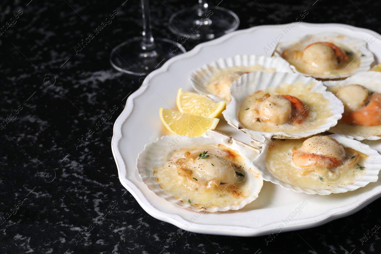 Photo of Fried scallops in shells and lemon on black textured table, closeup. Space for text