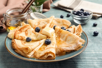 Photo of Thin pancakes with honey, berries and butter on plate, closeup