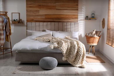 Bed with white knitted plaid in room. Interior design