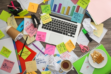 Photo of Laptop, notes and office stationery in mess on desk, top view. Overwhelmed with work