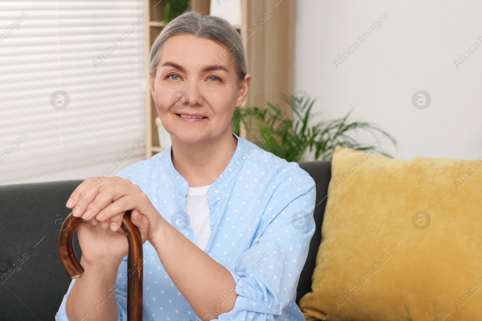 Photo of Senior woman with walking cane sitting on sofa at home. Space for text