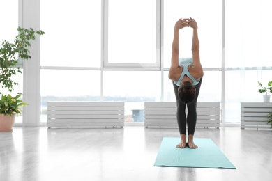 Photo of Young woman practicing standing forward bend with shoulder opener asana in yoga studio. Uttanasana pose