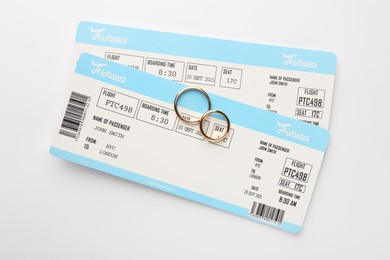 Photo of Honeymoon concept. Plane tickets and two golden rings on white background, top view