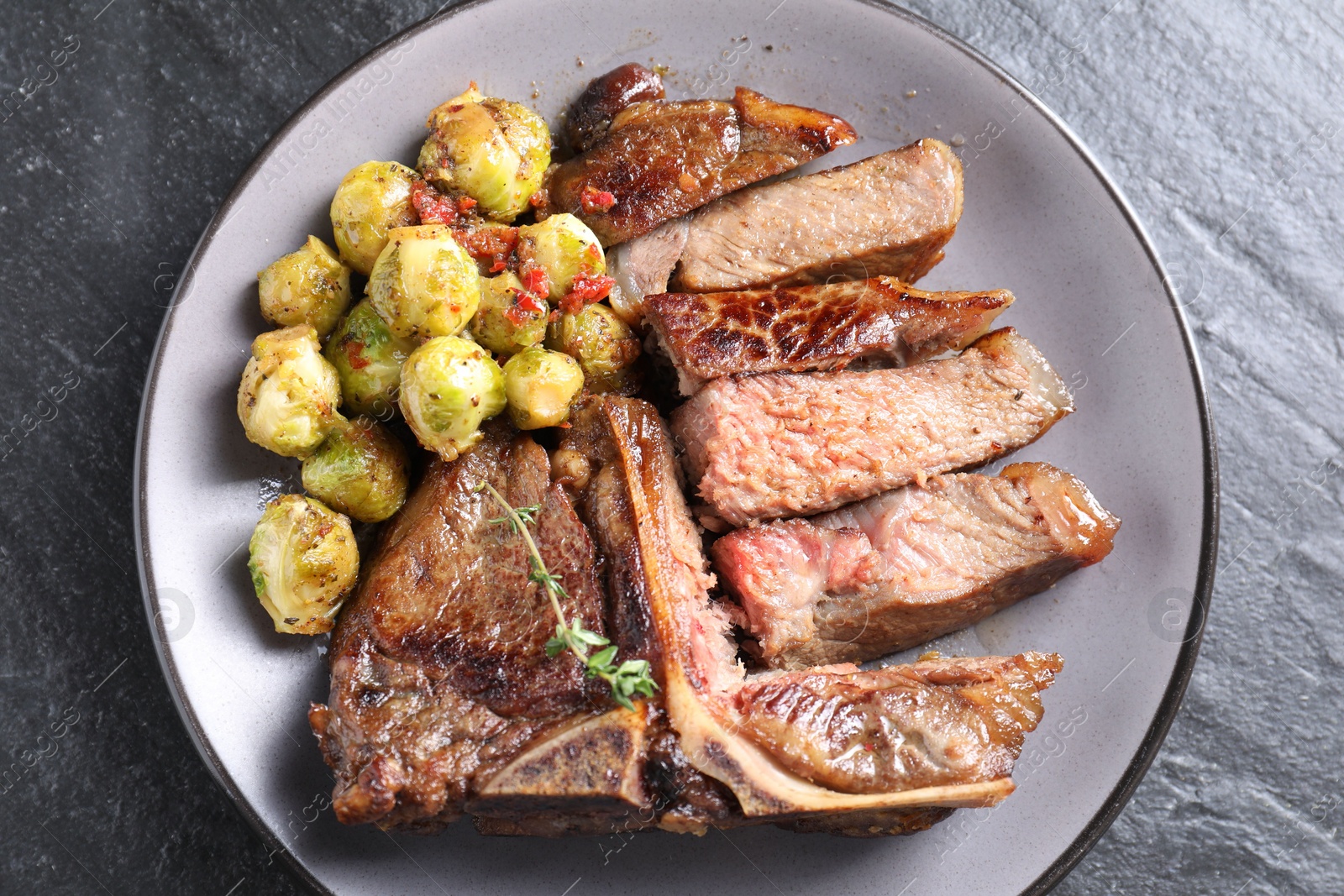 Photo of Delicious fried beef meat, vegetables and thyme on black table, top view