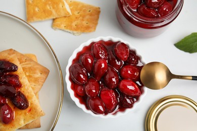 Delicious dogwood jam with berries and crispy crackers on white table, flat lay