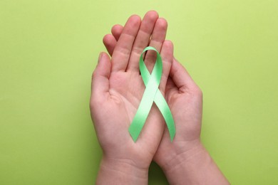 World Mental Health Day. Woman holding green ribbon on color background, top view