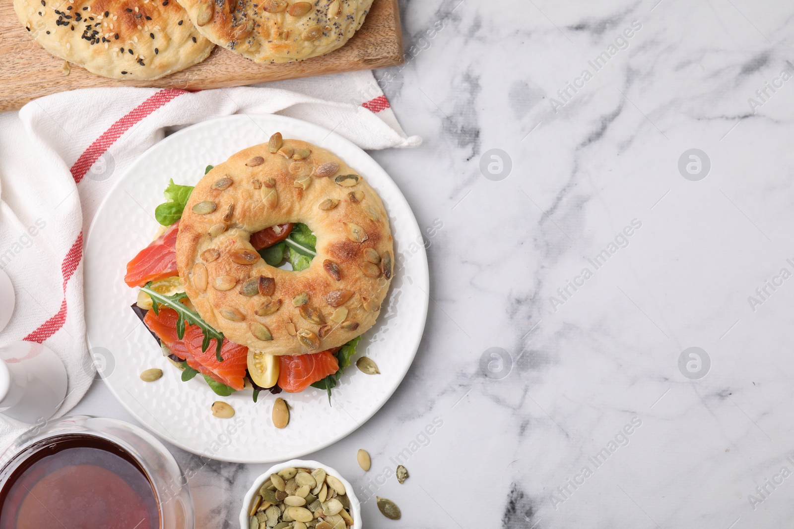 Photo of Tasty bagel with salmon and tomatoes on white marble table, flat lay. Space for text