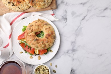 Tasty bagel with salmon and tomatoes on white marble table, flat lay. Space for text