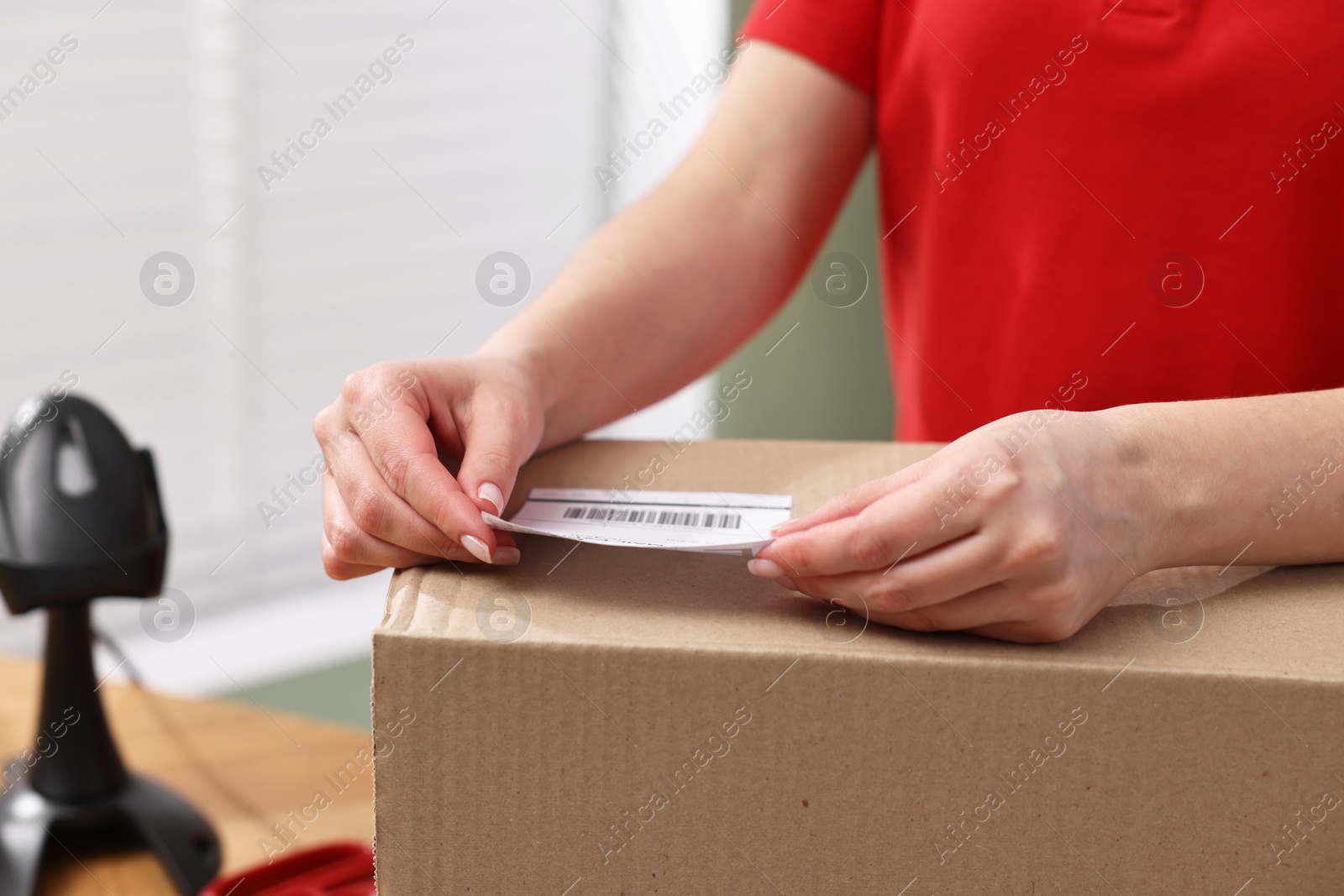 Photo of Parcel packing. Post office worker sticking barcode on box indoors, closeup