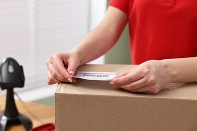 Photo of Parcel packing. Post office worker sticking barcode on box indoors, closeup