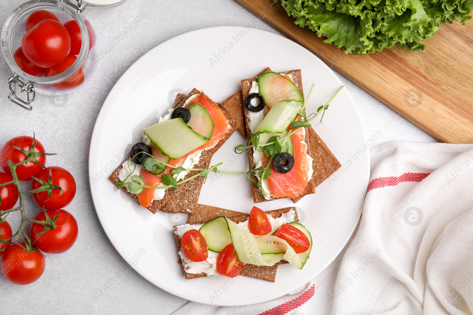 Photo of Tasty rye crispbreads with salmon, cream cheese and vegetables served on light grey table, flat lay