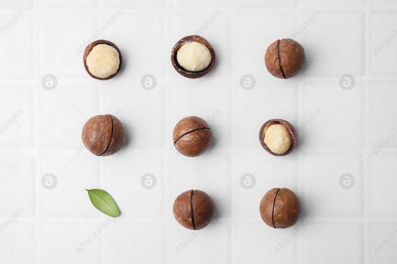 Photo of Tasty Macadamia nuts and green leaf on white background, flat lay