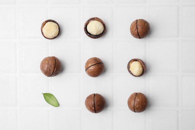 Tasty Macadamia nuts and green leaf on white background, flat lay