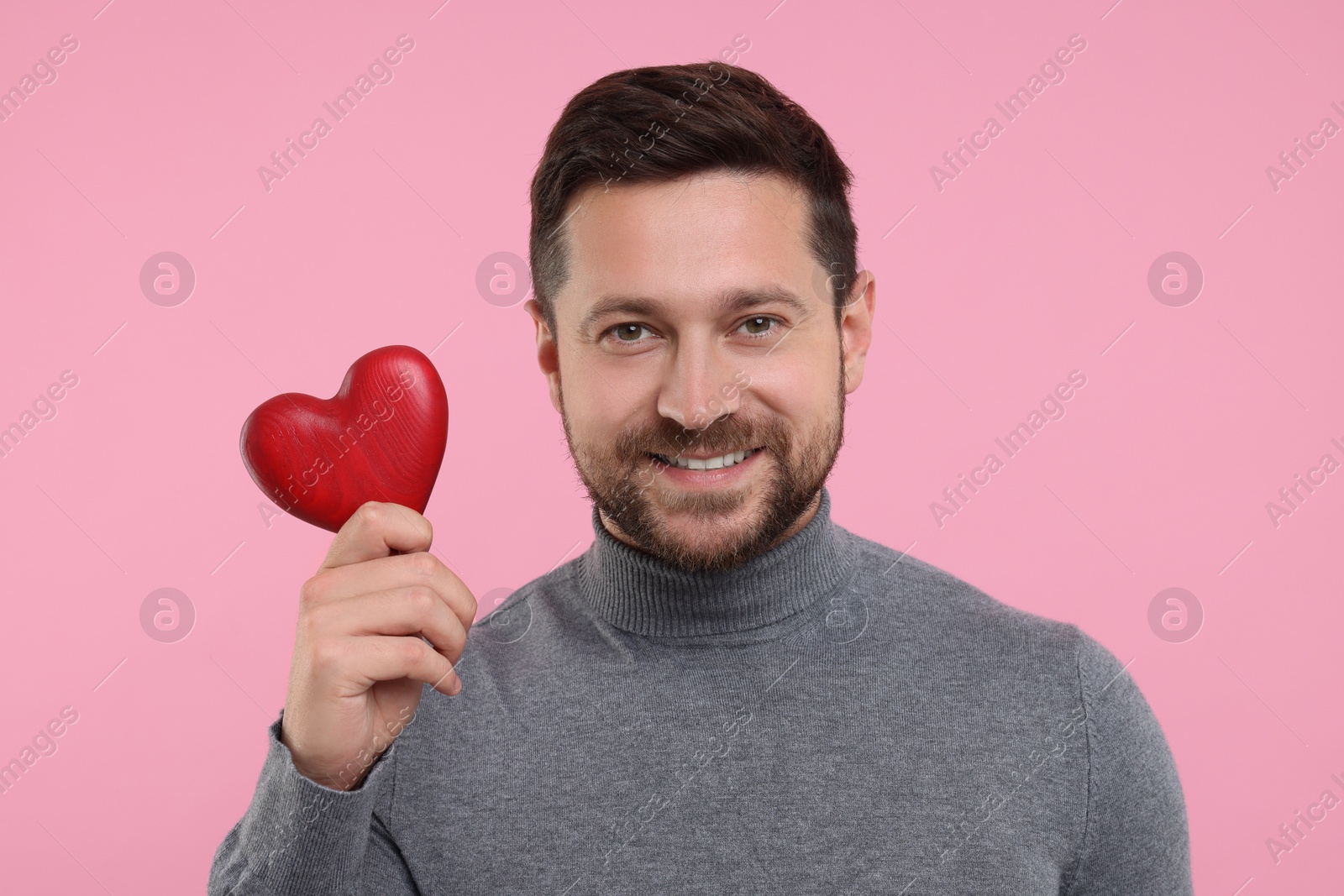 Photo of Happy man holding red heart on pink background