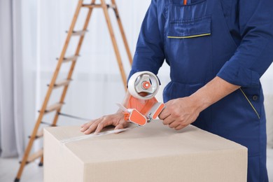 Photo of Male mover packing box with adhesive tape in house, closeup