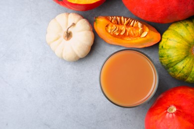 Photo of Tasty pumpkin juice in glass and different pumpkins on light grey table, flat lay. Space for text
